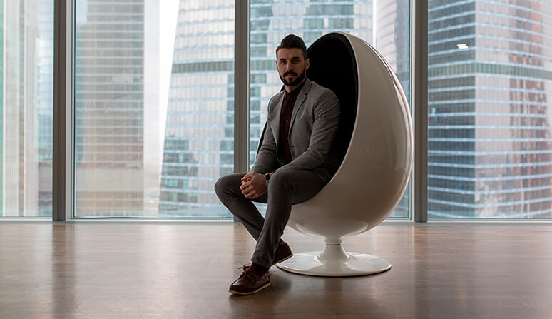 Business man wearing a grey suit sitting in modern white Egg Chair with buildings in the background